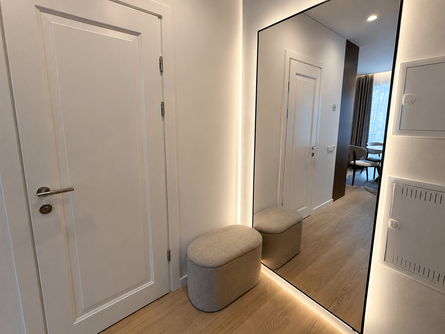 Modernus apartamentų prieškambaris su nenideliu pufu ir apšviestu veidrodžiu ant sienos